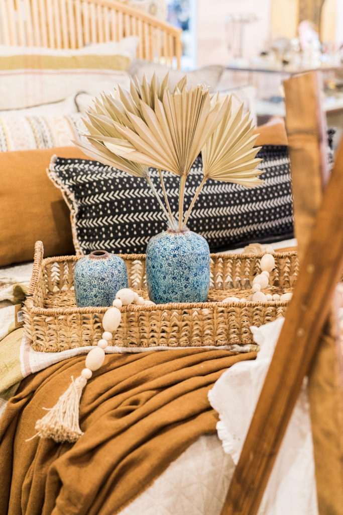 The Designer's Garage boho chic decor in retail space at from 6th collective featuring dried palms, vases, bedding, and home decor.