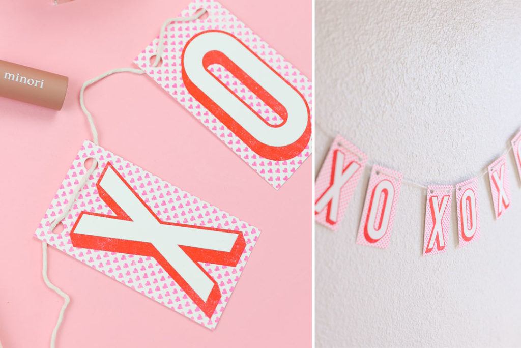 Screen printed paper banner on white cotton twine with red typography and hearts of XOXO love kisses and hugs baner on pink background. Home Decor party banner party supplies gift shop.