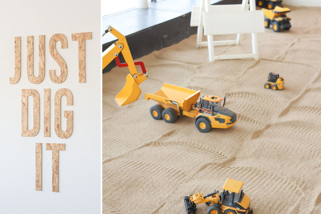 Just Dig It sign made out of unpainted chip board, next to a picture of tonka trucks, cranes, and tractors in a large sand pit or sandbox. Just Dig It kid's children's play room