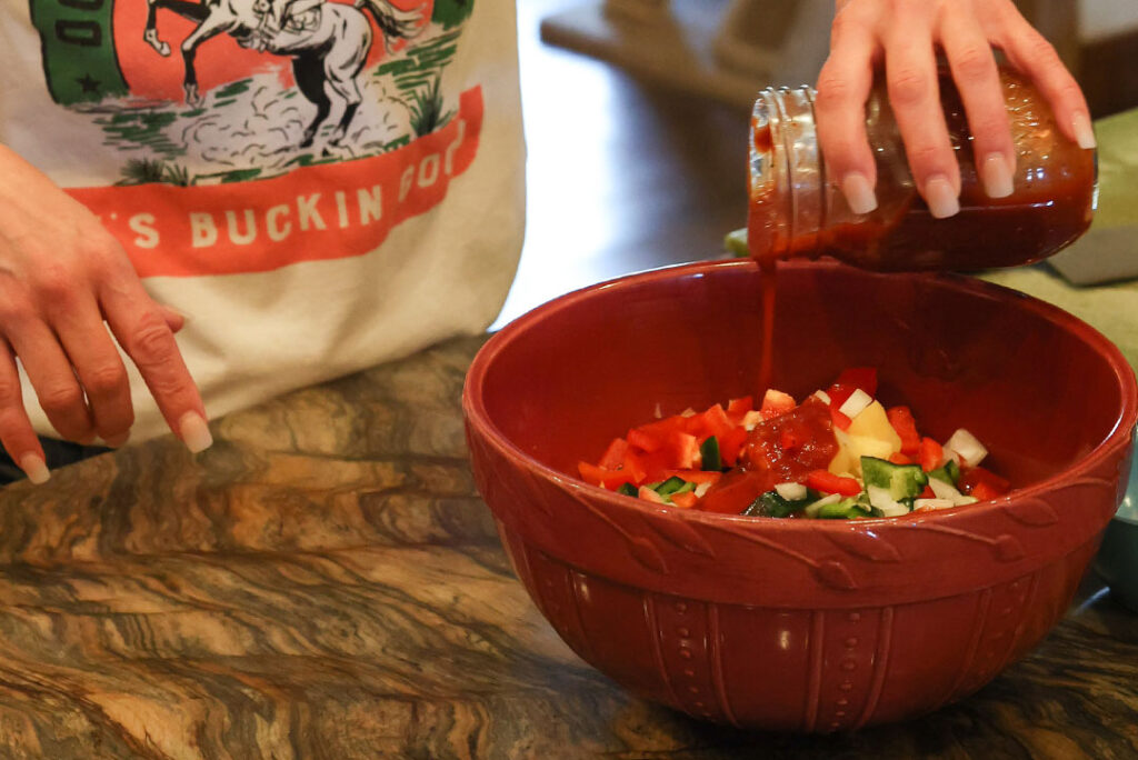 Pouring extra dove creek barbecue sauce in bowl with other vegetables in tex mex recipe